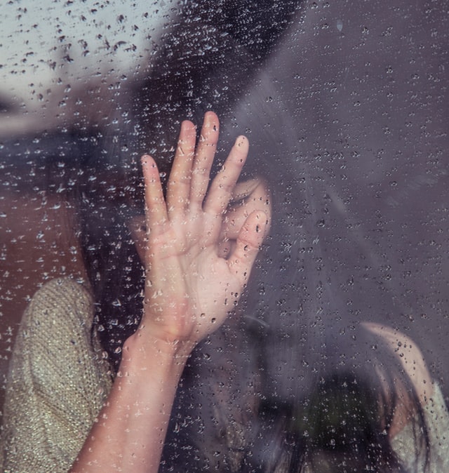 woman looking out window while it is raining